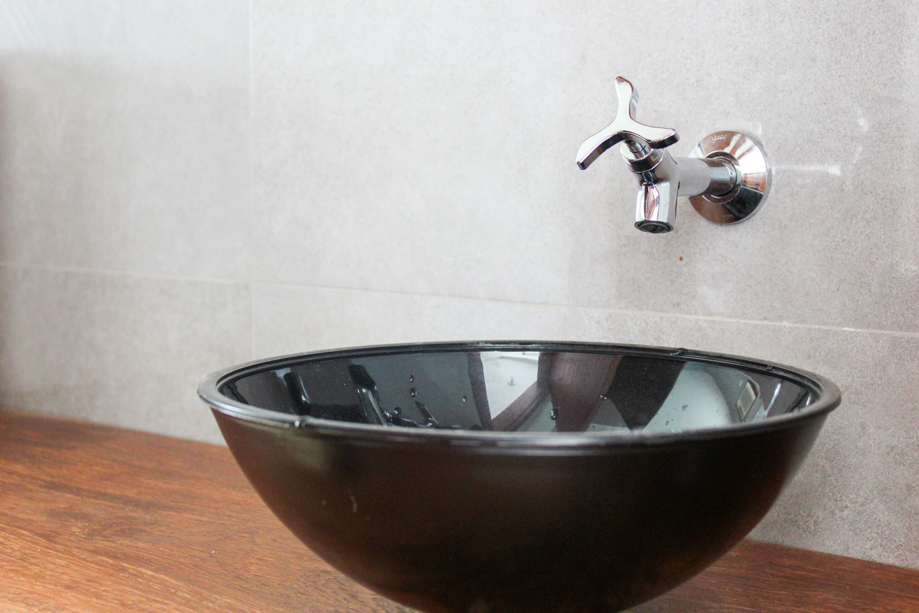 Une salle de bain moderne avec un lavabo en verre noir et un robinet chromé fixé sur un mur carrelé.