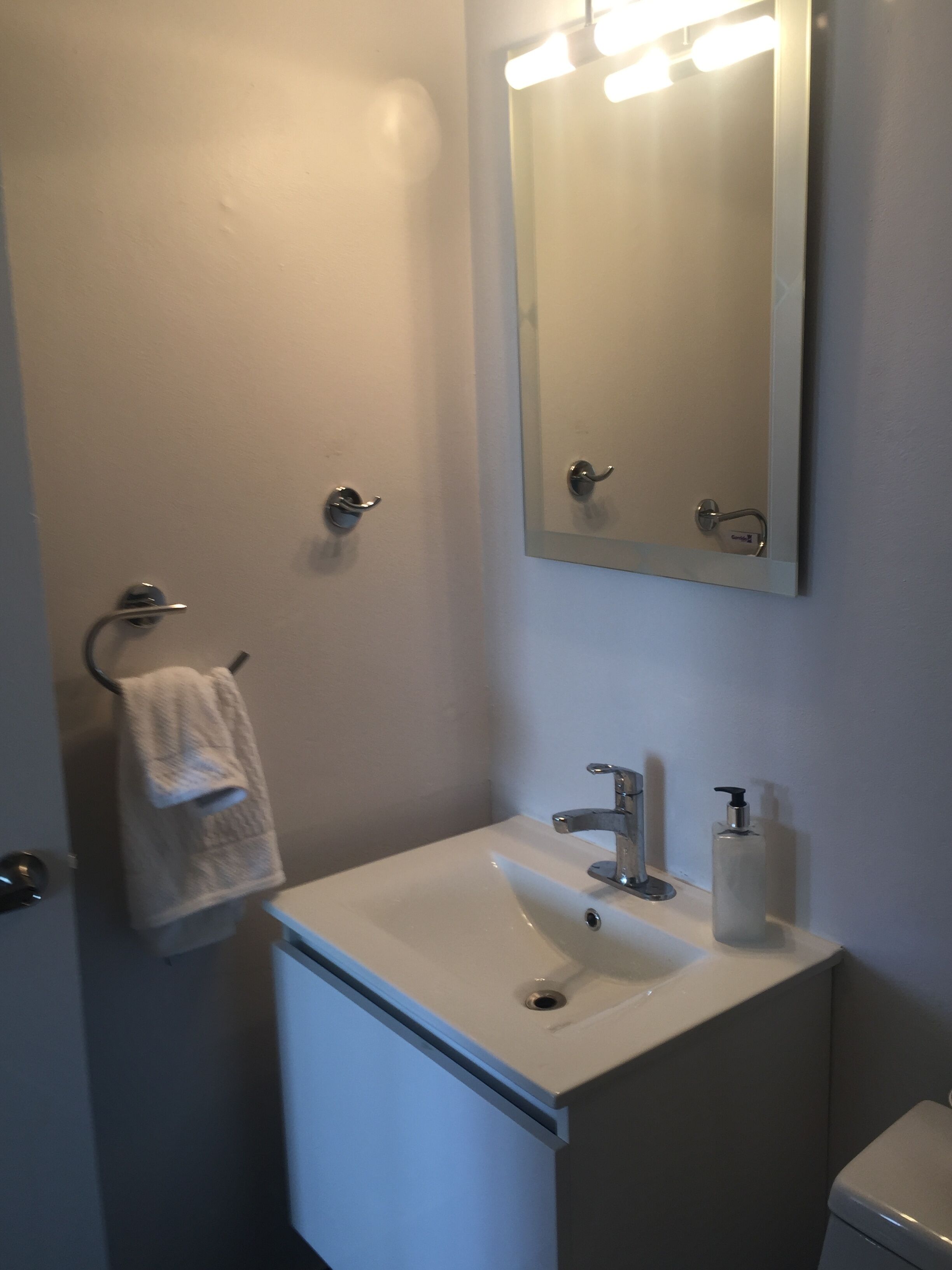 Une salle de bain avec un lavabo blanc, un miroir, un porte-serviettes et des toilettes.