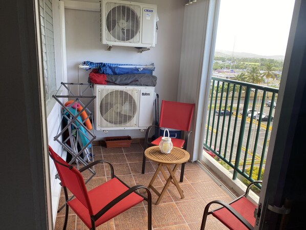 A balcony with two red chairs, a small round table, and two air conditioning units.