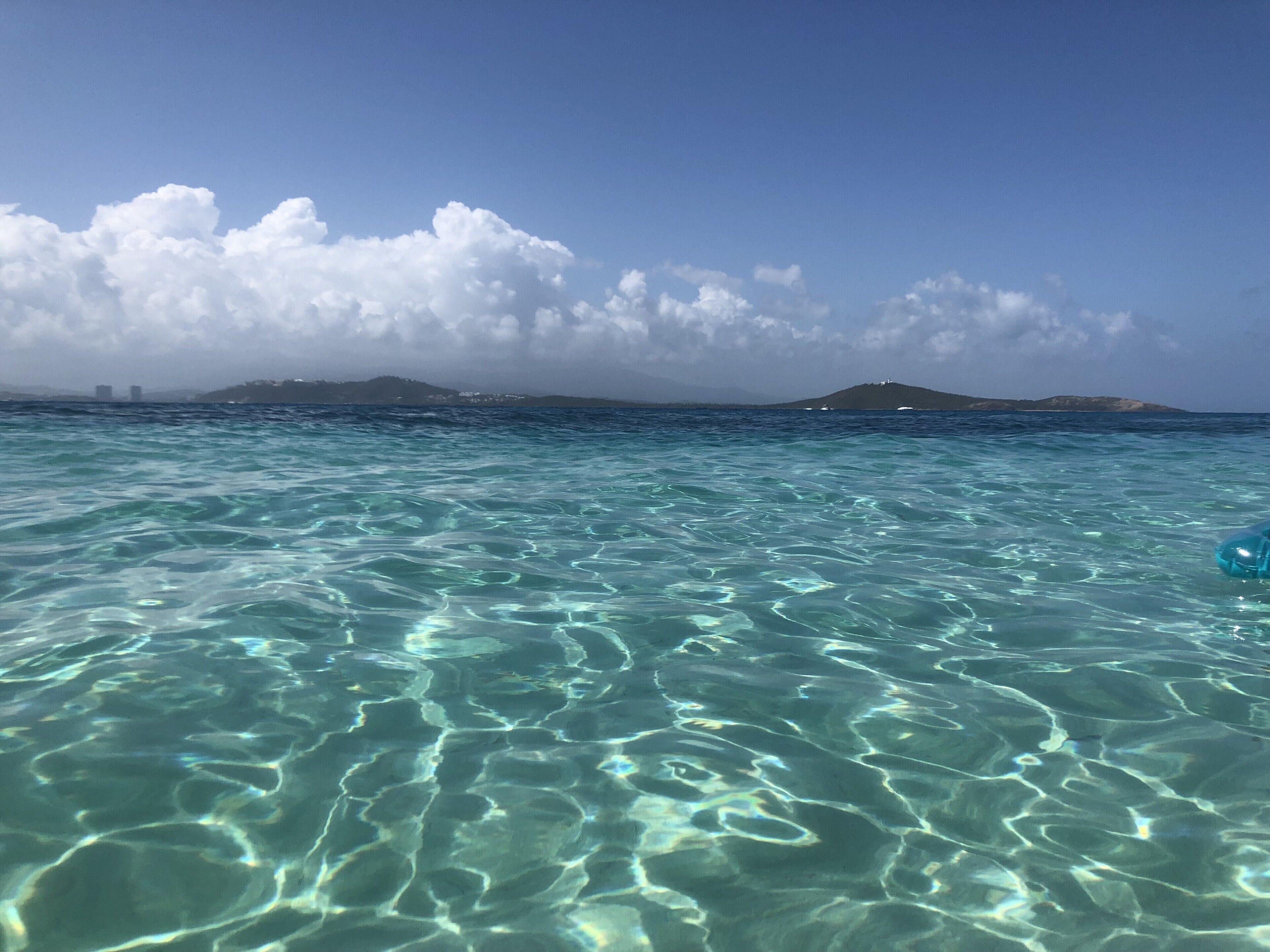 Clear turquoise sea water with visible ripples and a distant island with buildings.