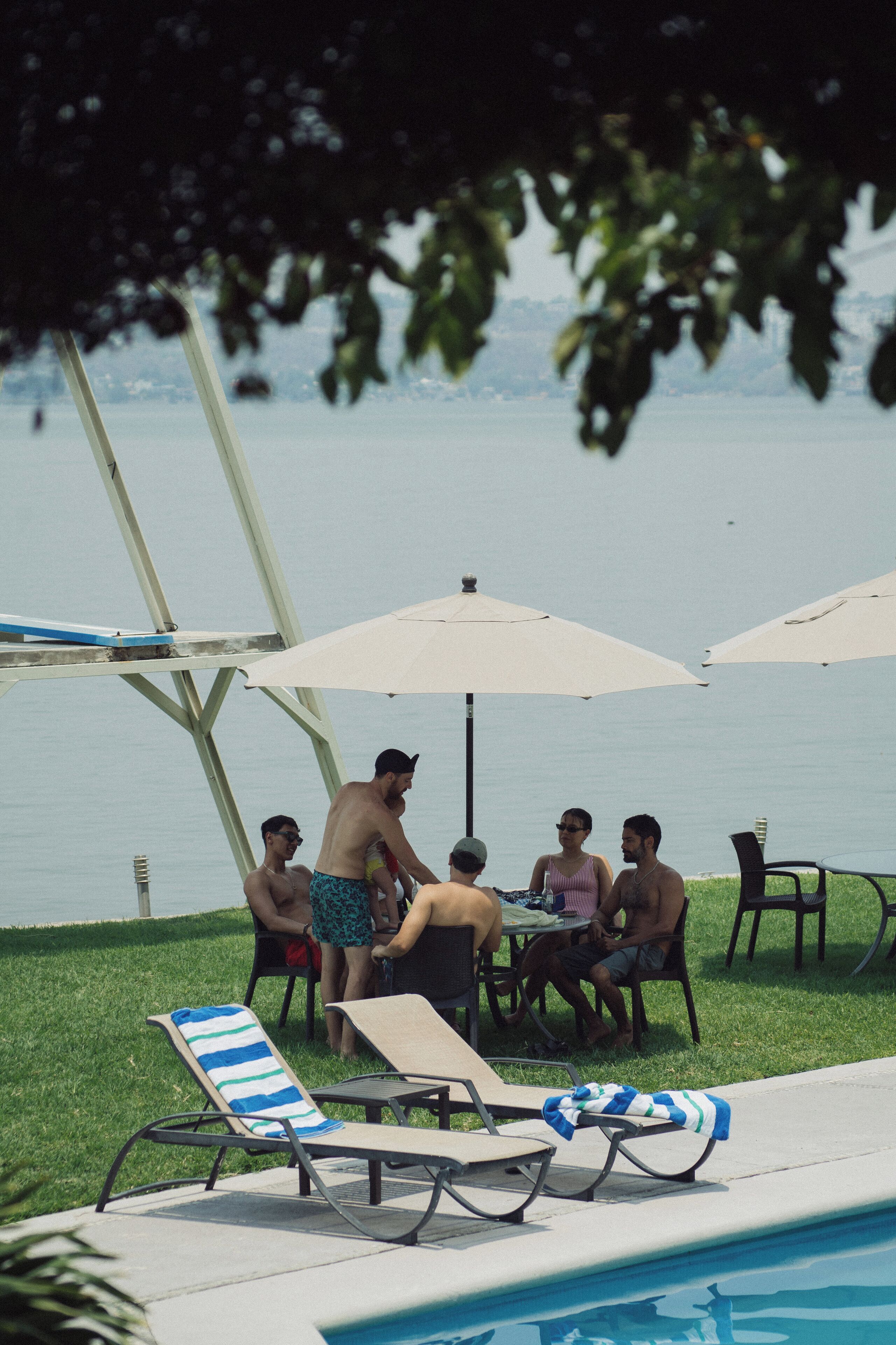 Ein Poolbereich mit Liegestühlen, Sonnenschirmen und einem Tisch, an dem sich Personen befinden.