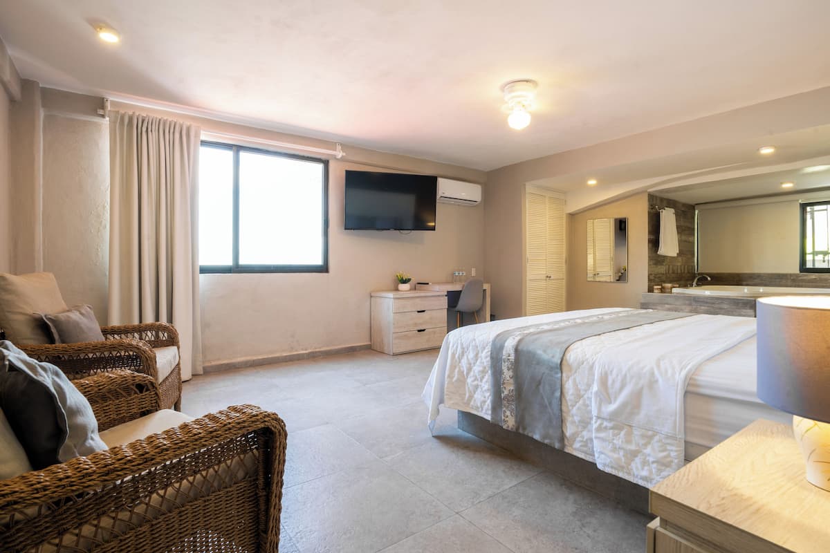 Ein Schlafzimmer mit Bett, Schreibtisch, Stuhl, Fernseher und einem Badezimmer mit Spiegel und Waschbecken.