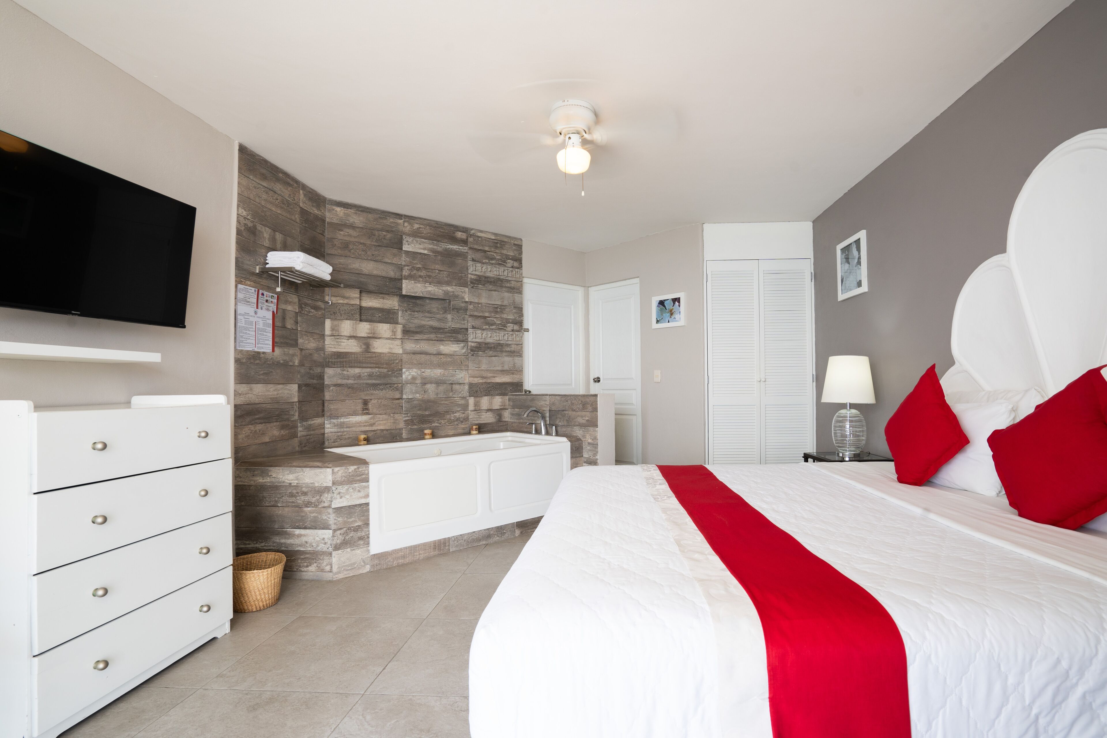 A modern bedroom with a large bed, a built-in TV, a vanity with a mirror, and a stone accent wall.