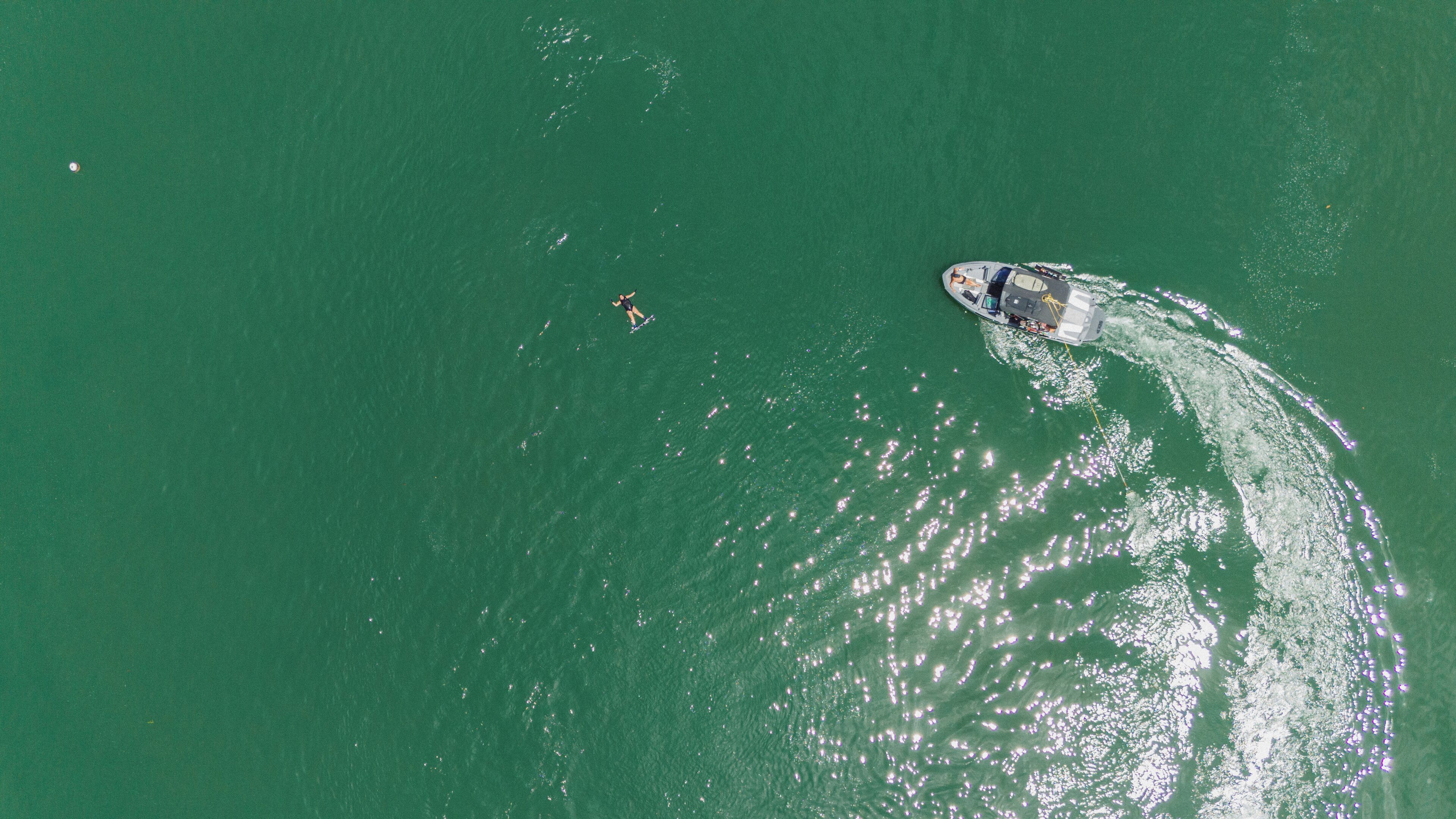 An aerial view of a boat on a greenish body of water with wake patterns.