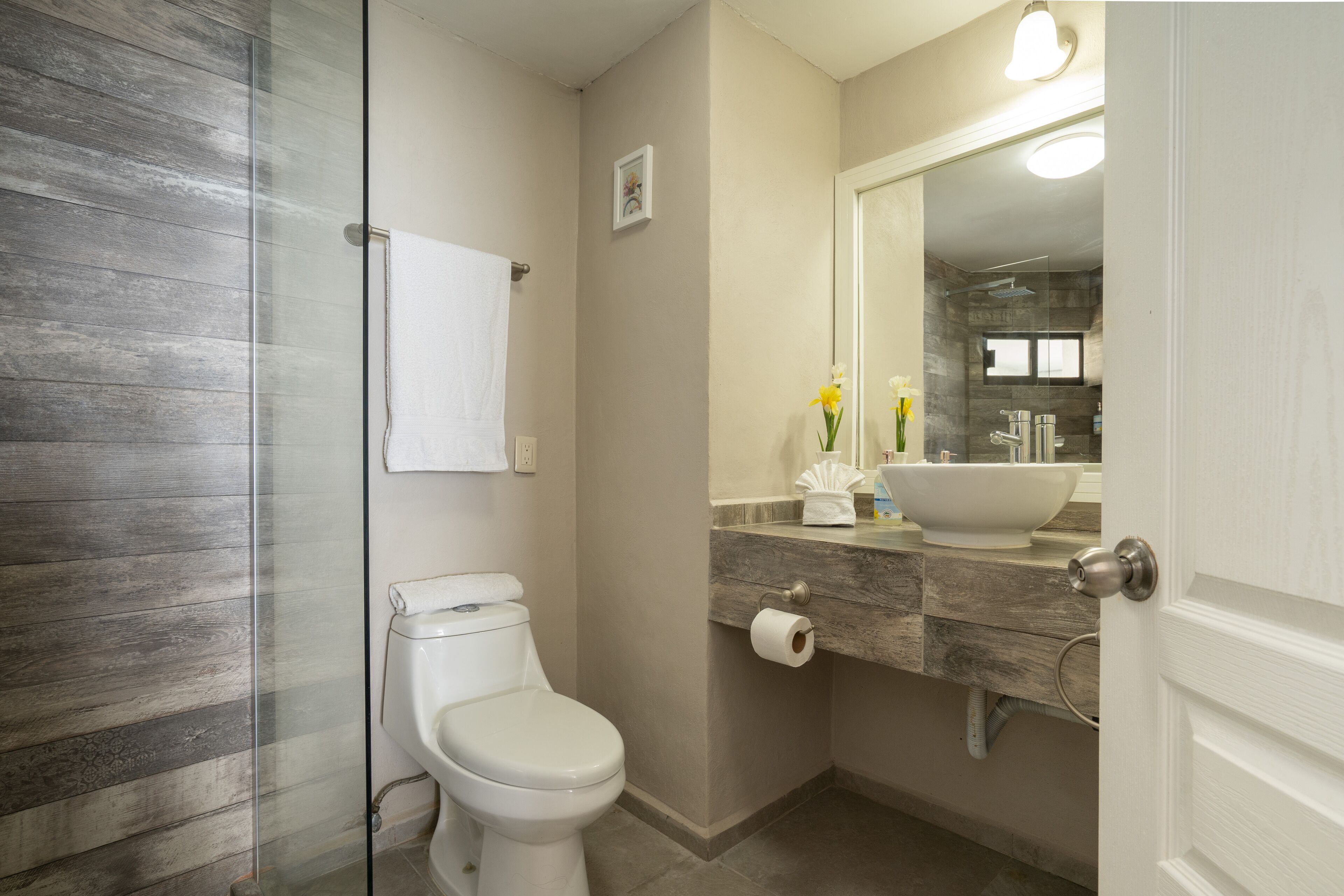 Een badkamer met toilet, een douchecabine van glas, een wastafel met een spiegel en een handdoekrek.