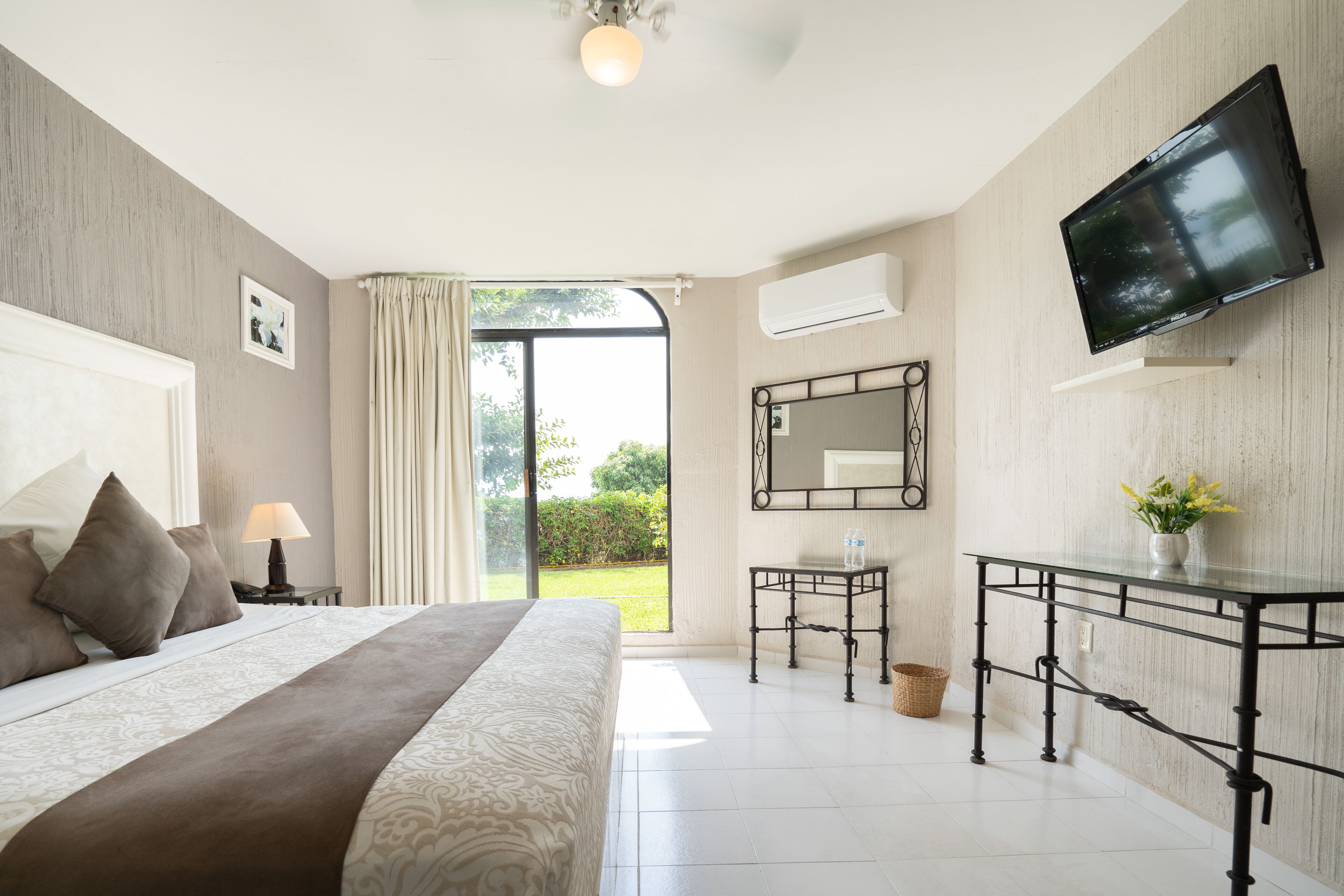 Une chambre à coucher avec un lit, un bureau, une télévision et une fenêtre avec des rideaux.