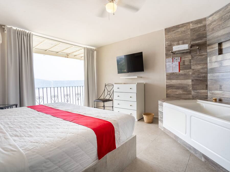 A hotel room with a bed, a TV, a bathroom with a bathtub, and a view of the mountains.