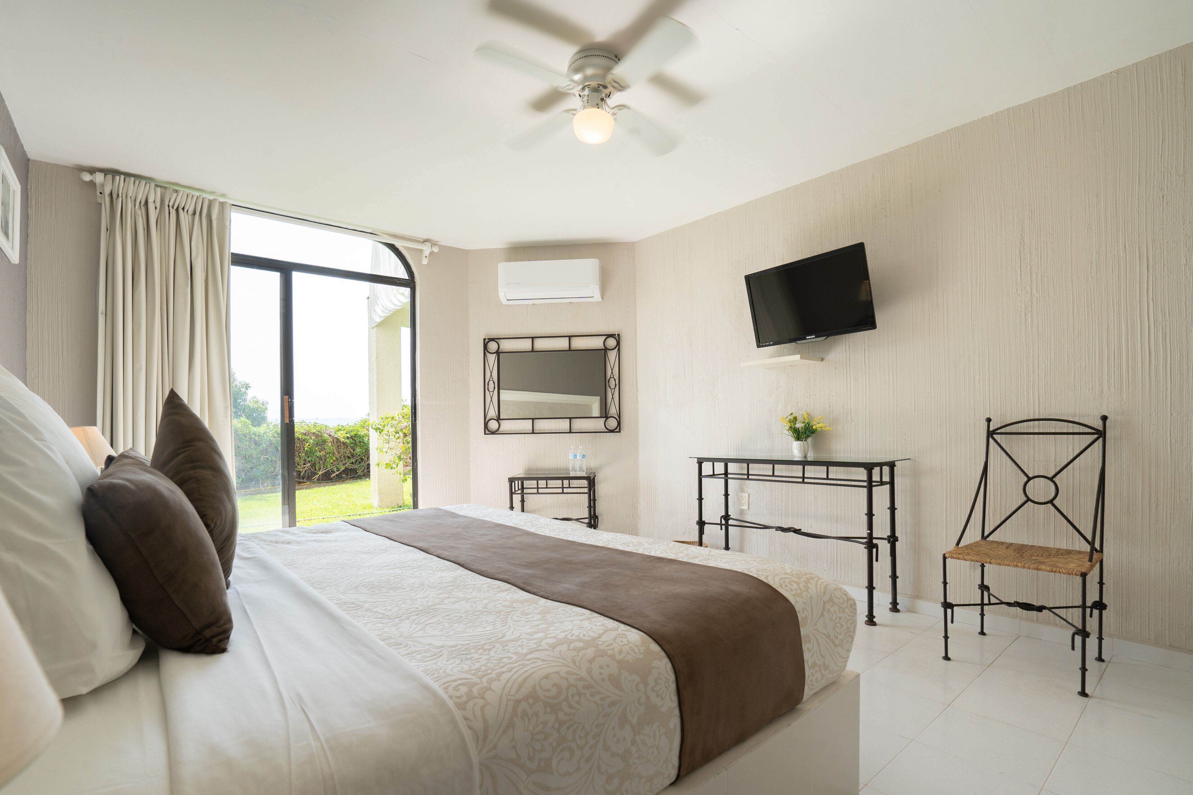 Un dormitorio con cama, ventilador de techo, televisor, escritorio y silla.