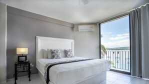 Ein Schlafzimmer mit einem großen Bett, einem Nachttisch mit Lampe, einer Klimaanlage und einem Balkon mit Aussicht.