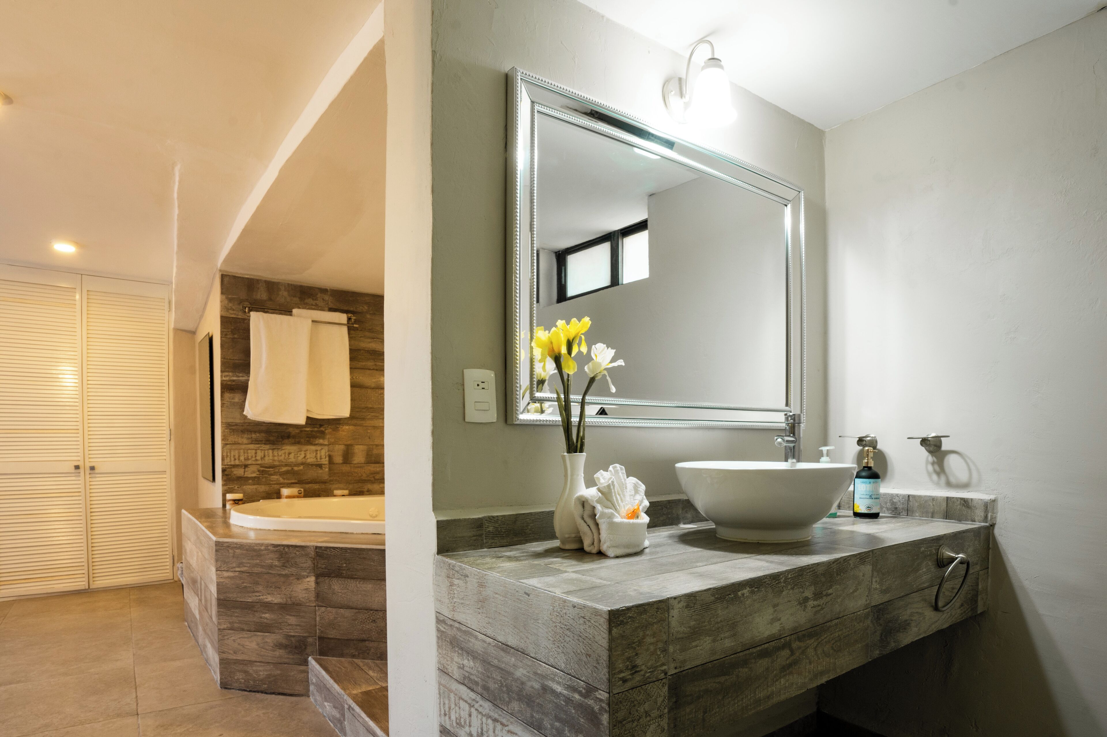 Un baño moderno con un espejo grande, una bañera y un tocador con lavamanos y toallero.