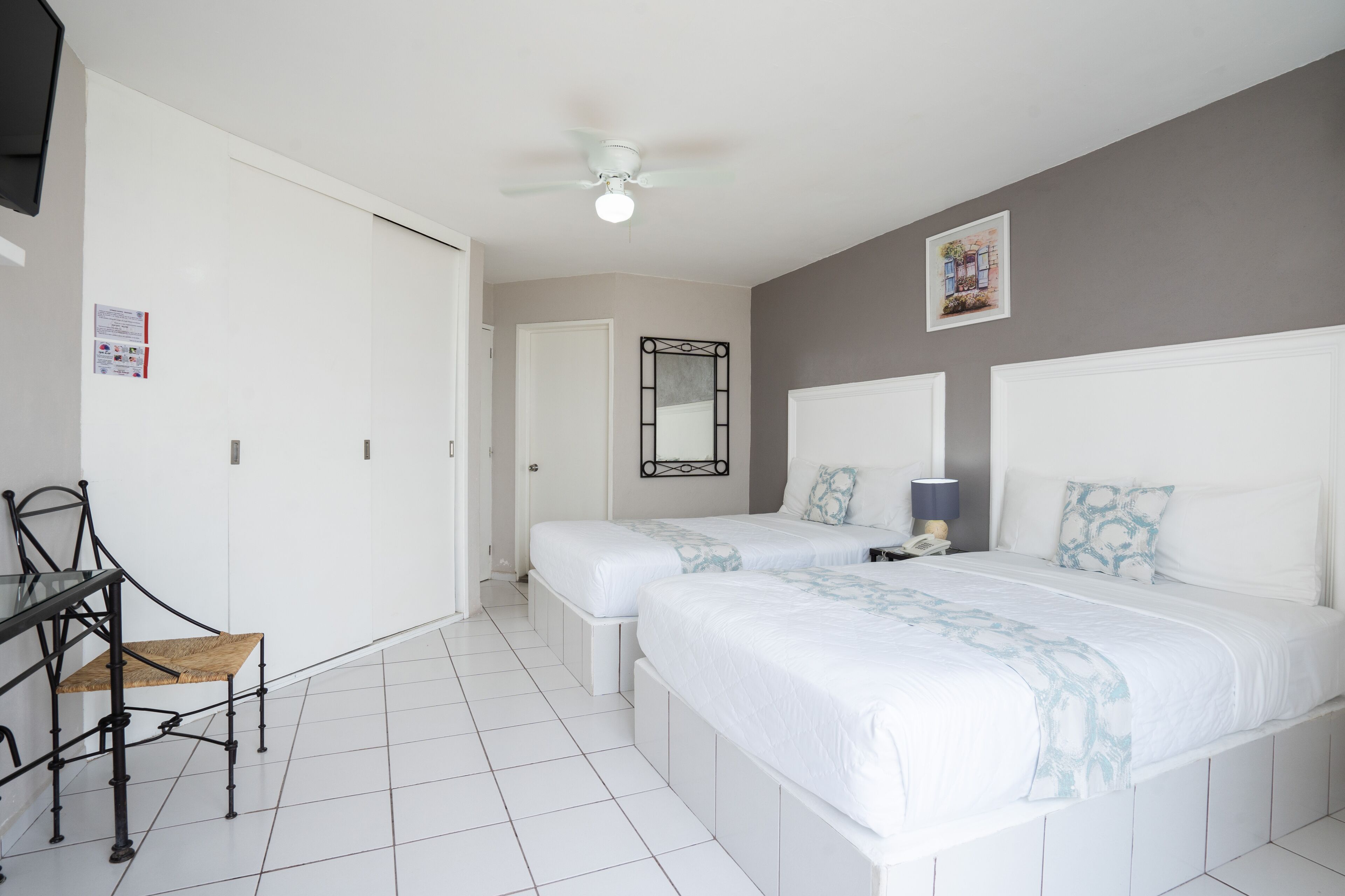 A bedroom with two beds, a ceiling fan, a desk with a chair, and a mirror on the wall.