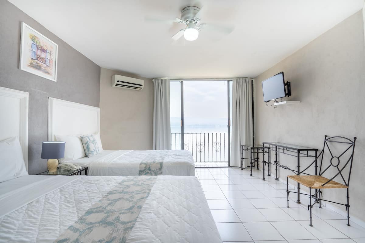 Ein Hotelzimmer mit zwei Betten, einem Deckenventilator, einem Fernseher, einem Balkon mit Geländer und einem kleinen Tisch mit Stühlen.
