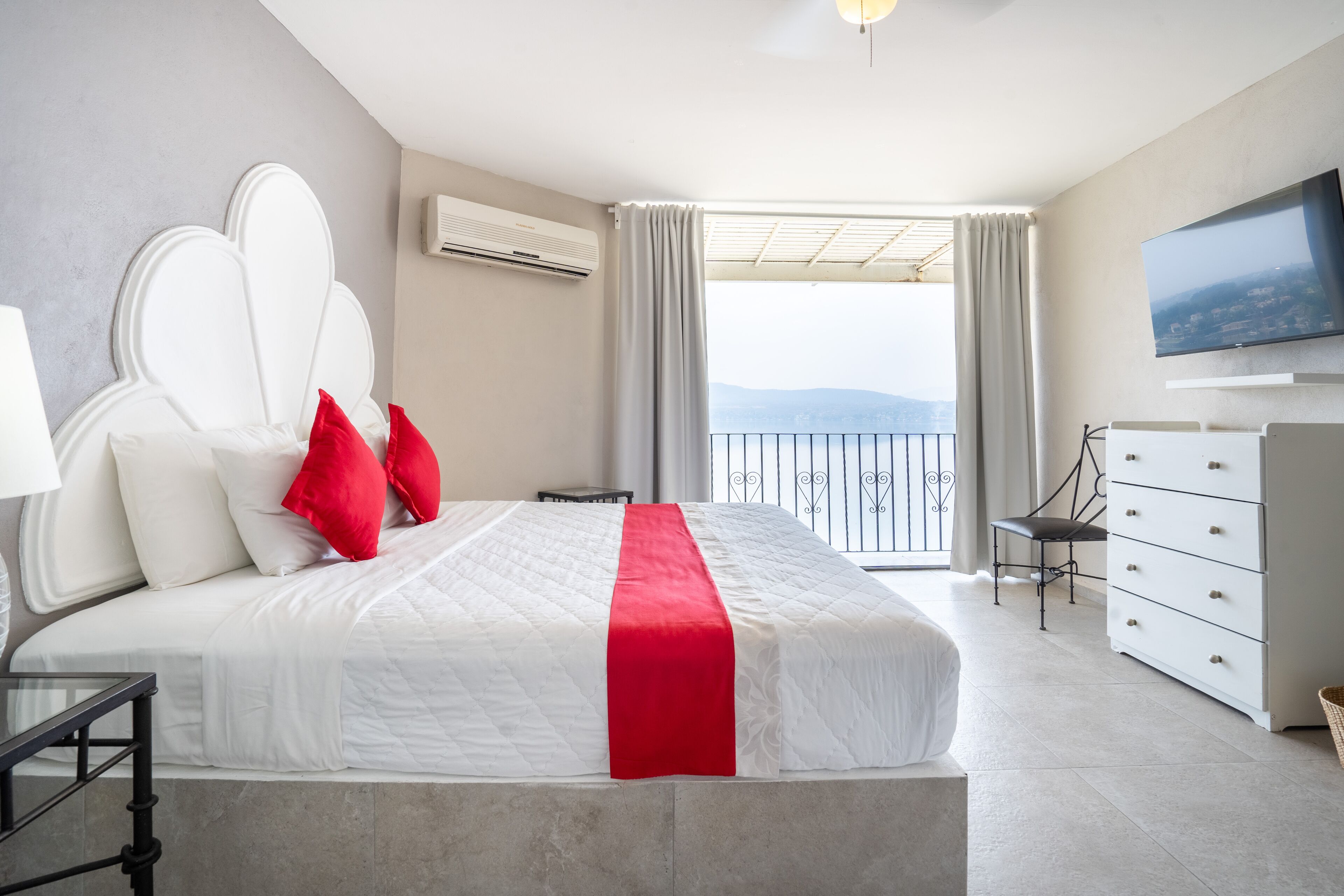 A modern hotel room with a large bed, a TV, a dresser, and a balcony with a view.
