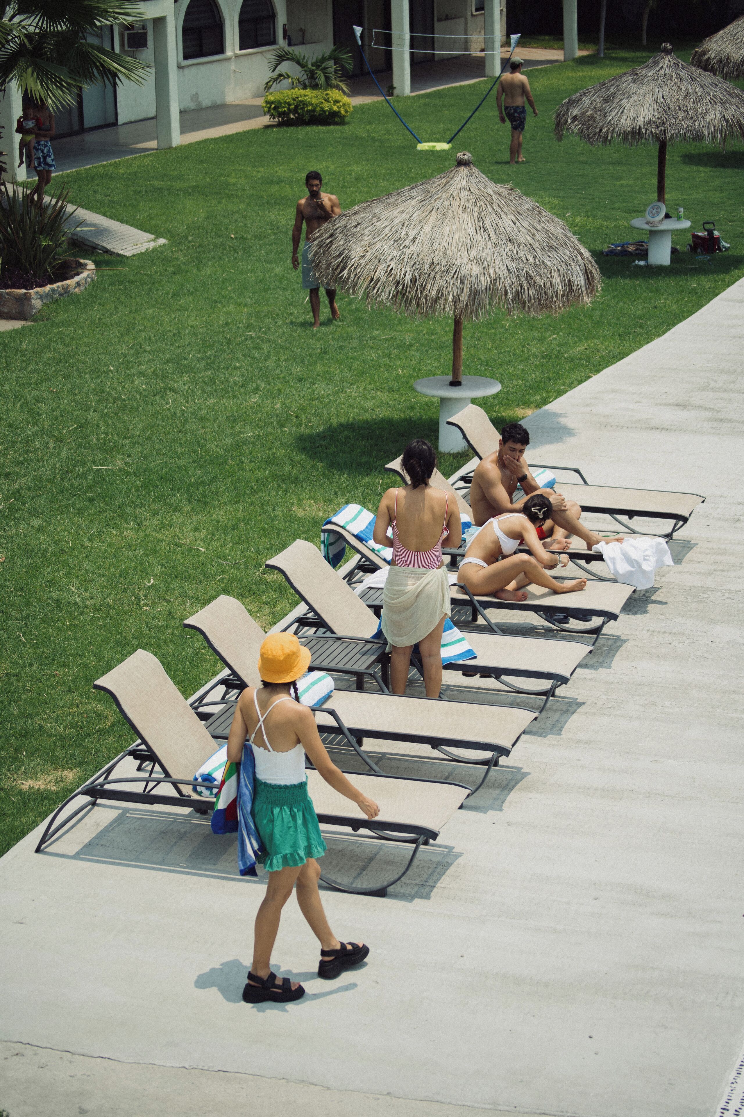 Un espace aménagé au bord de la piscine, avec des chaises longues, un palmier et un parasol en feuilles de palmier.