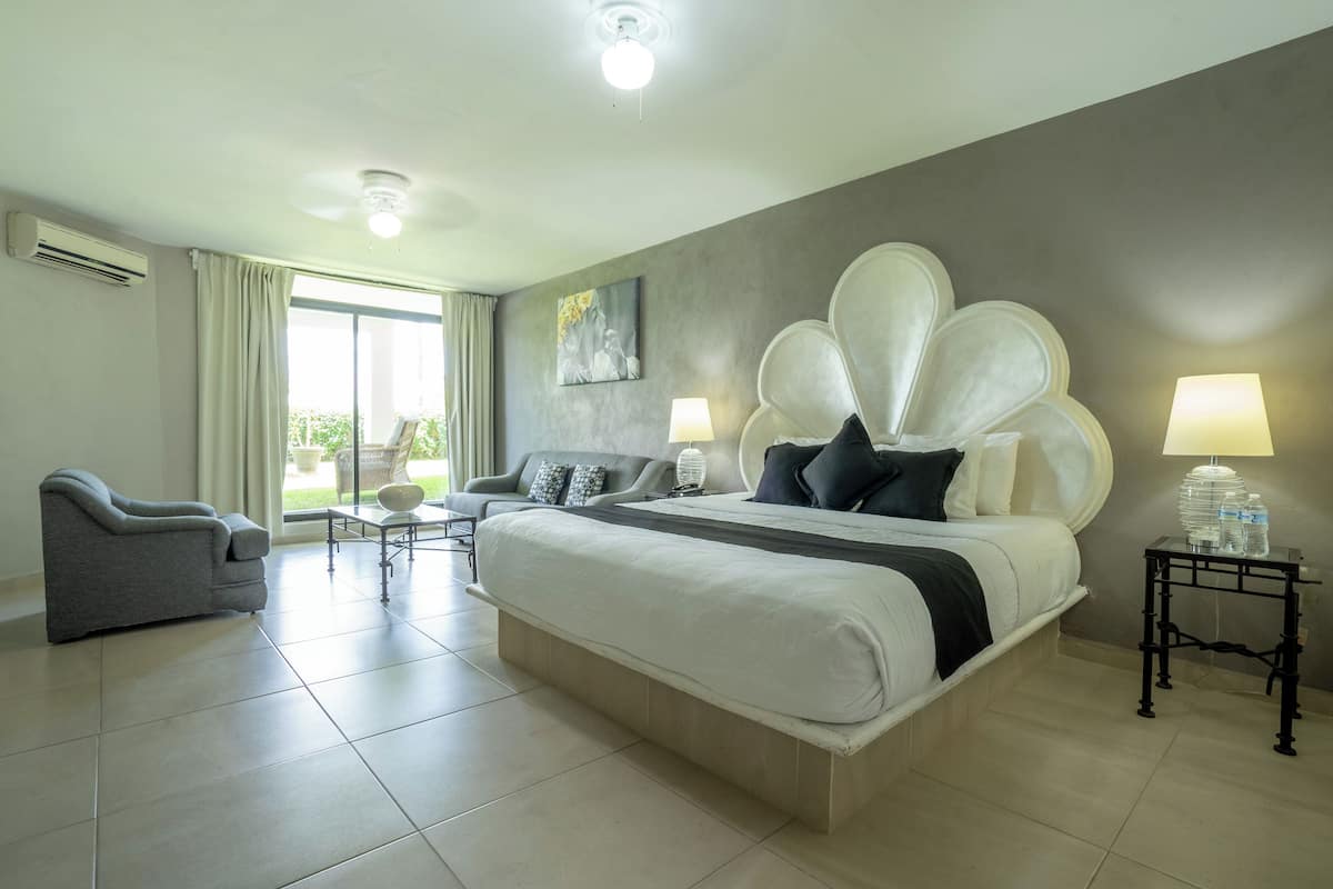 Ein Hotelzimmer mit einem großen Bett, einem grauen Sessel, einem kleinen Tisch und einer Lampe.