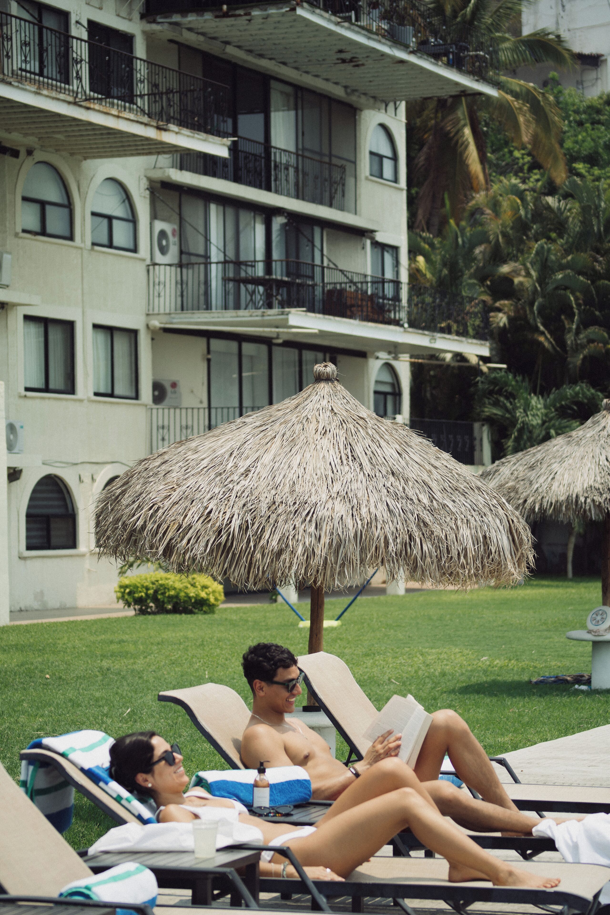 A hotel with a pool area, lounge chairs, and thatched umbrellas.