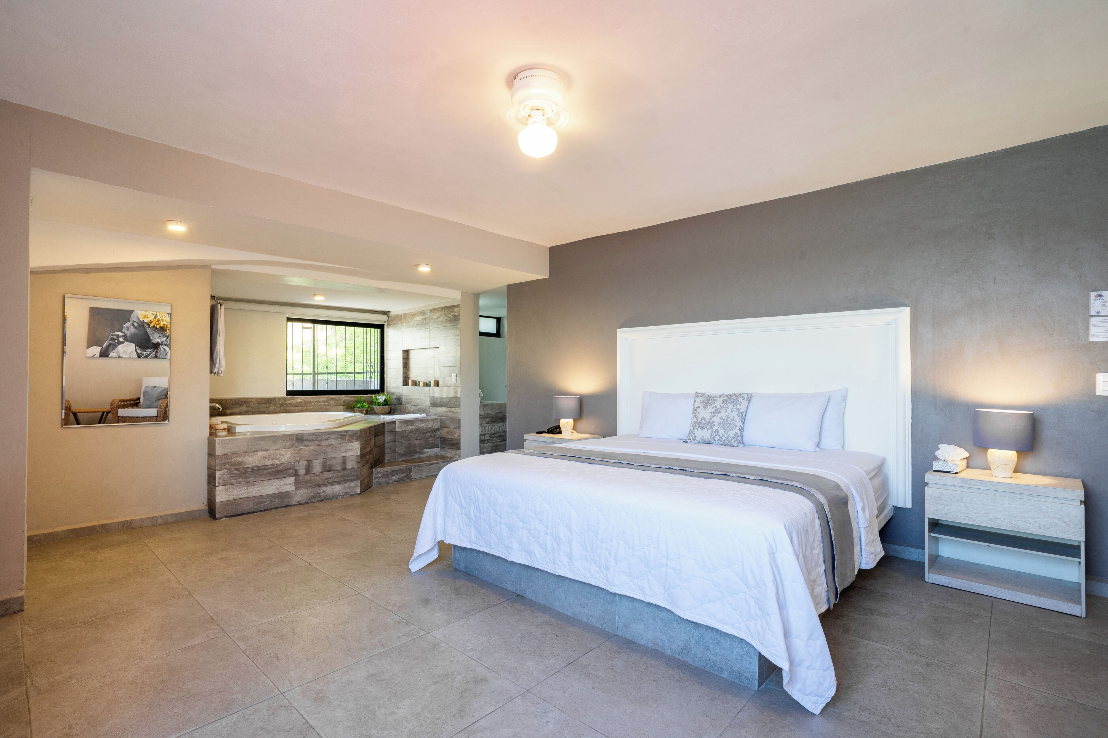 Une chambre à coucher moderne avec un grand lit, des tables de chevet, une commode et une salle de bain équipée d’un lavabo et d’un miroir.