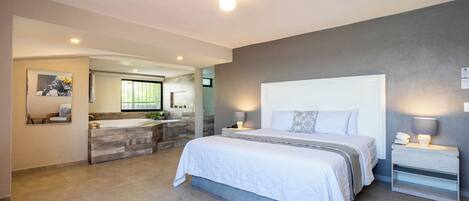 Une chambre à coucher moderne avec un grand lit, des tables de chevet, une commode et une salle de bain équipée d’un lavabo et d’un miroir.