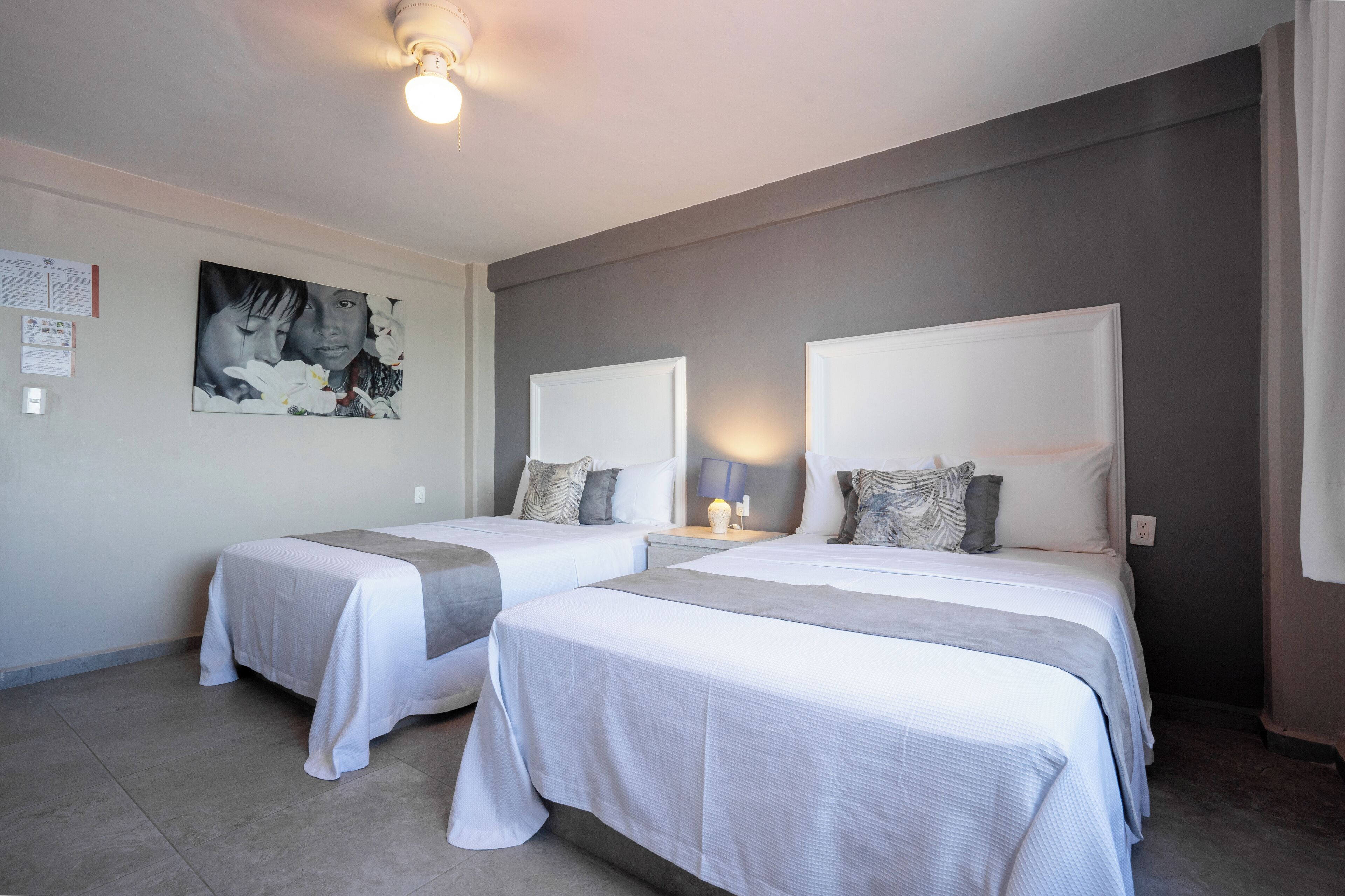 A hotel room with two beds, a painting on the wall, and a ceiling light.