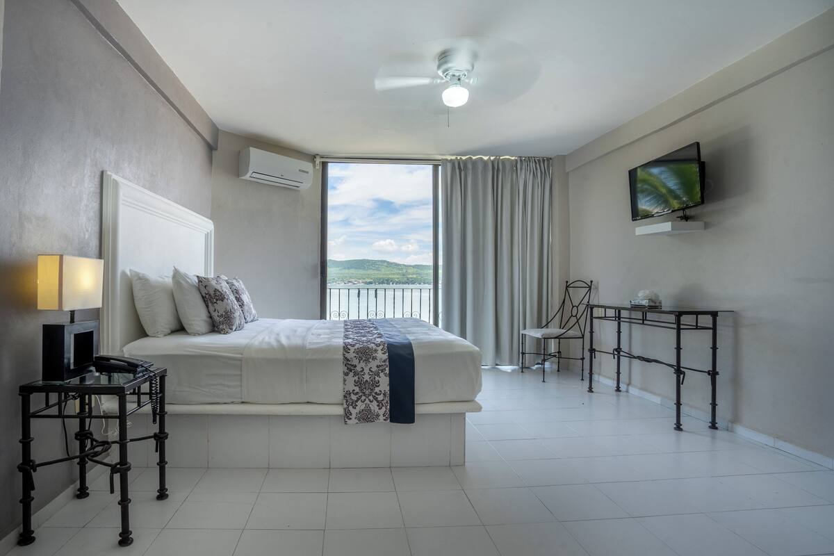 Ein Hotelzimmer mit Bett, Schreibtisch, Stuhl, Fernseher und Blick ins Freie.