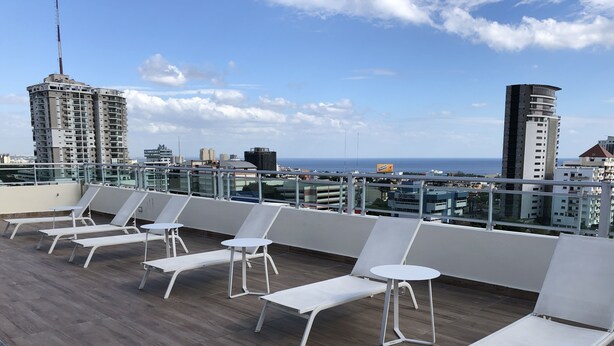 A rooftop lounge with white lounge chairs and a view of the city skyline and ocean. - Rooftop Pool with Ocean and City Views (Santo Domingo)