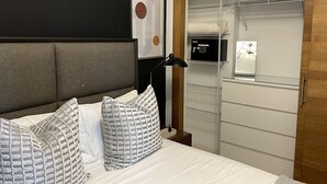 A bedroom with a bed, pillows, a bedside lamp, a wardrobe, and a framed artwork on the wall. - Rooftop Pool with Ocean and City Views (Santo Domingo)