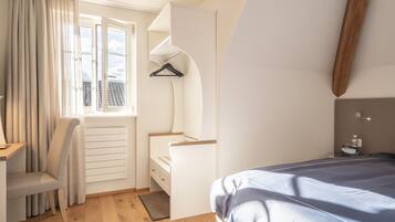 A bedroom with a bed, a desk, a chair, a hanging coat rack, and a window with curtains.