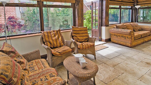 A sunroom with wicker furniture, large windows, and a view of greenery. - 3 bedroom accommodation in Whitby (Whitby)