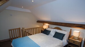 A bedroom with a bed, wooden headboard, nightstands, and a sloped ceiling. - 3 bedroom accommodation in Whitby (Whitby)