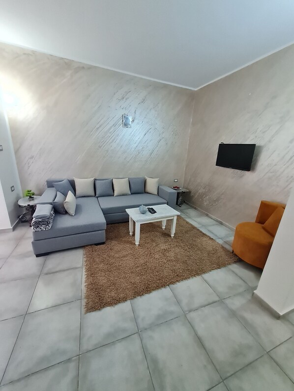 A modern living room with a grey sectional sofa, a white coffee table, a brown rug, and a small orange chair.