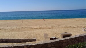 Una playa con un muro de piedra en primer plano, cielo azul despejado y mar tranquilo.