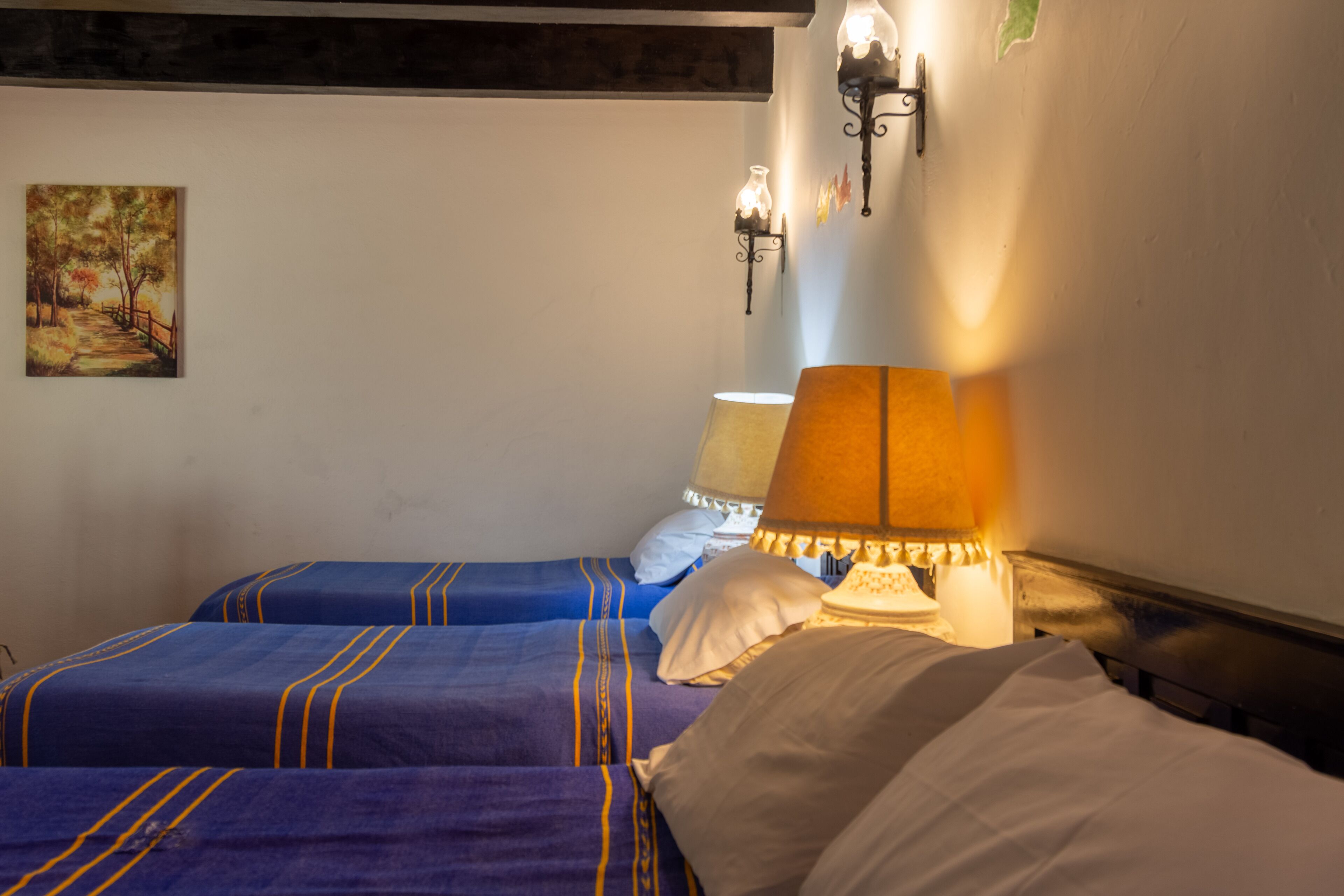 Una habitación de hotel con dos camas, cada una con ropa de cama azul y un cabecero de madera. Hay un cuadro en la pared y una lámpara en la mesita de noche.