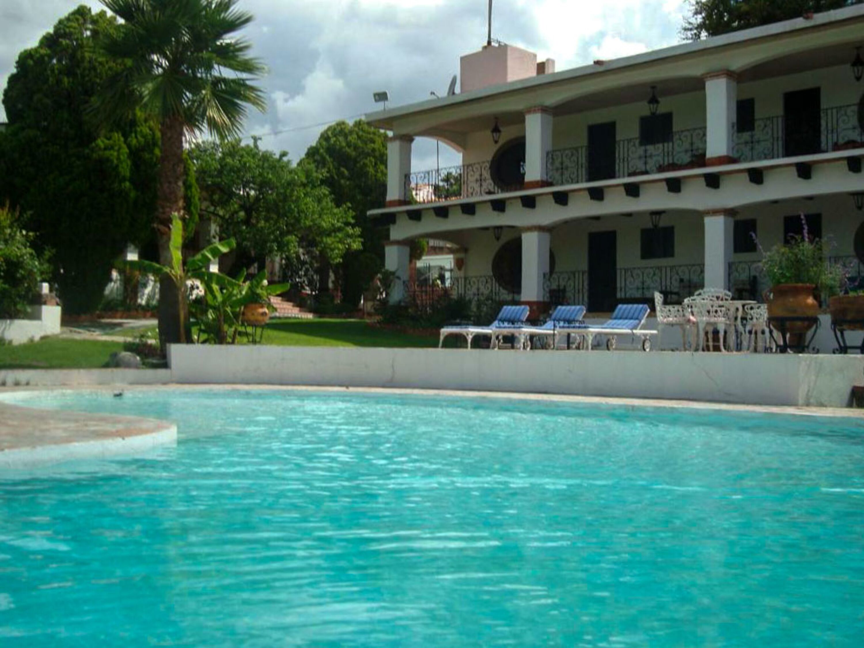 Una piscina con sillones de descanso y un edificio con balcones al fondo.