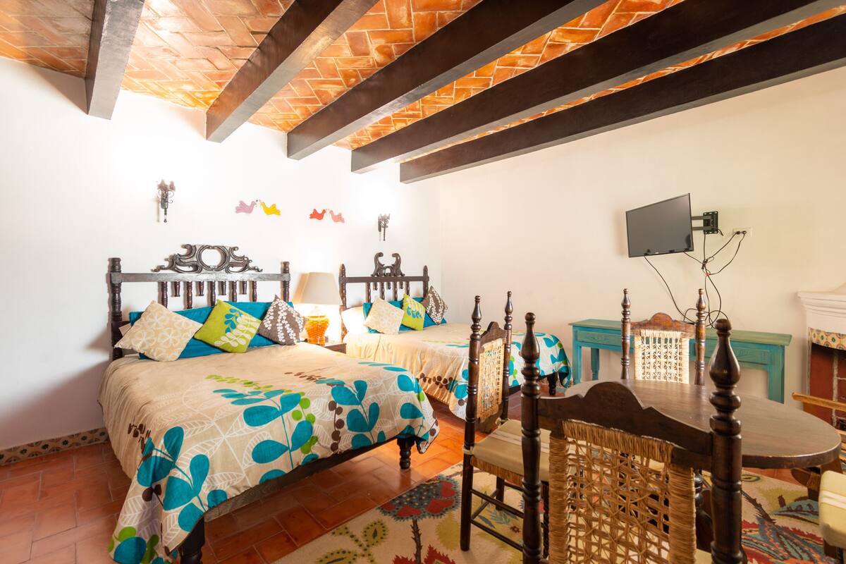 Una camera da letto con un letto, una sedia di legno, un tavolo e una TV a muro.