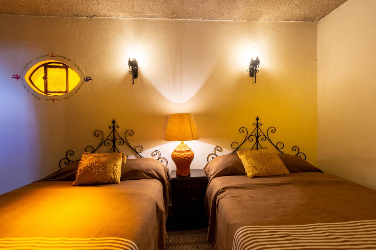 Una stanza con due letti, un comodino, una lampada e applique.