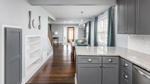 A modern kitchen with grey cabinets, a granite countertop, and a wooden floor. - Cozy Downtown Greenwood Retreat - Walkable to Everything (Greenwood)