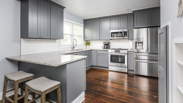 A modern kitchen with grey cabinets, a stainless steel refrigerator, and a central island with stools. - Cozy Downtown Greenwood Retreat - Walkable to Everything (Greenwood)