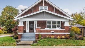 A two-story brick house with a gabled roof, white trim, and a front porch. - Cozy Downtown Greenwood Retreat - Walkable to Everything (Greenwood)