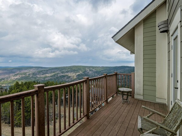 A wooden deck with a railing, a table, and a chair, overlooking a mountainous landscape.