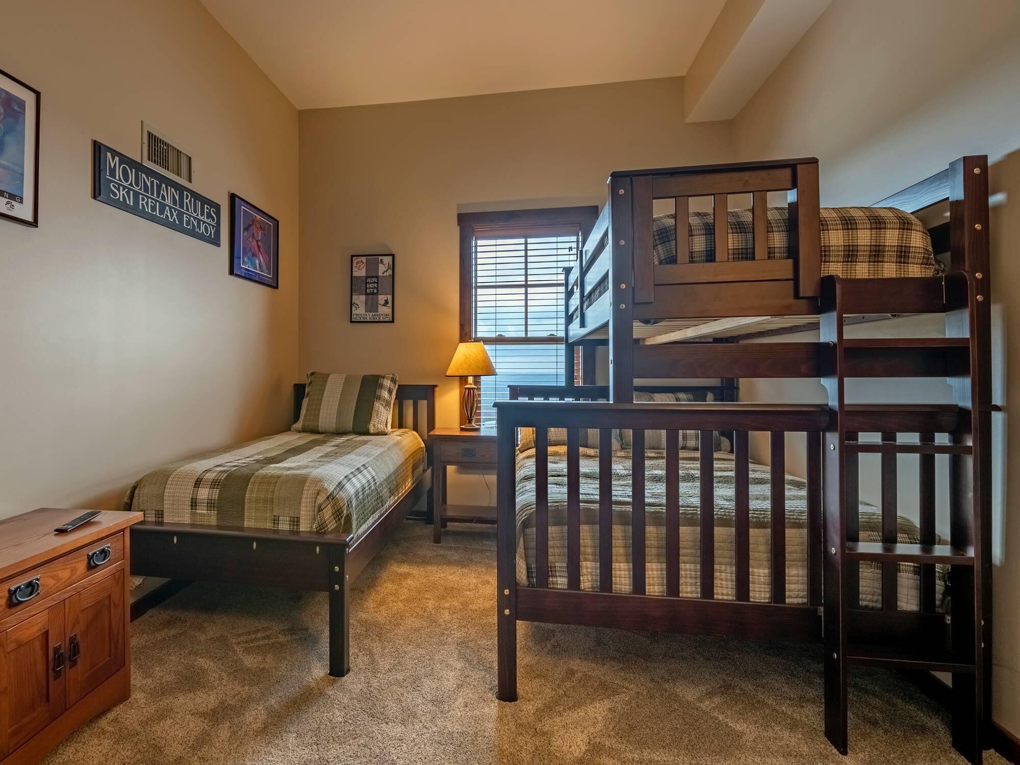 A bedroom with bunk beds, a bedside table, a lamp, and a dresser.