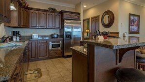 A modern kitchen with dark wood cabinets, stainless steel appliances, a granite countertop, and a bar area with stools. - 5 Br: Black Bear Crossing #4 (Snowshoe)
