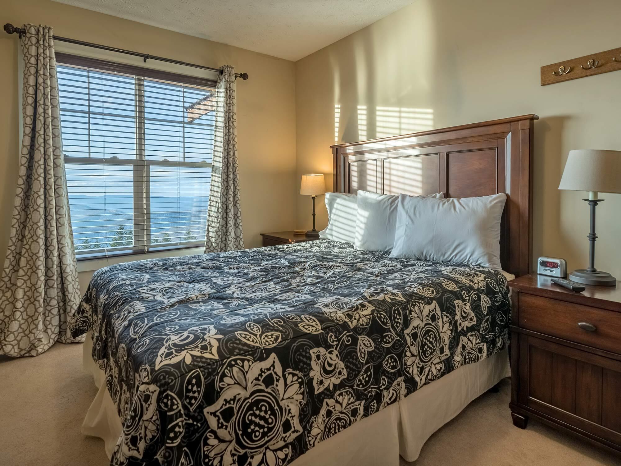A hotel room with a large bed, a nightstand with a lamp, a bedside table, and a window with curtains.
