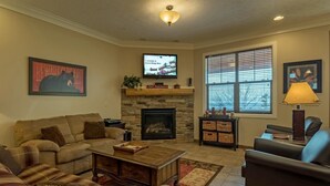 A living room with a stone fireplace, a television mounted above it, and a large window with blinds. - 5 Br: Black Bear Crossing #4 (Snowshoe)