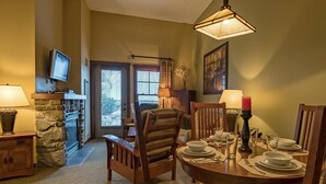 Un comedor con chimenea de piedra, sillas de madera, una mesa redonda para cuatro comensales y un televisor montado en la pared.