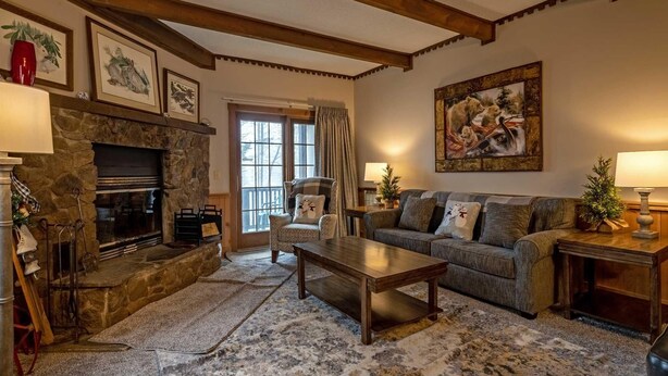 A cozy living room with a stone fireplace, a sofa, a coffee table, and a large painting on the wall. - 2 Br: Whistlepunk 28 (Snowshoe)