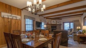 A dining area with a wooden table set for six, surrounded by chairs, a fireplace, and a television. - 2 Br: Whistlepunk 28 (Snowshoe)