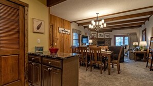 A spacious kitchen with wooden cabinets, a marble countertop, and a red bowl. There is a dining area with wooden chairs and a chandelier. - 2 Br: Whistlepunk 28 (Snowshoe)