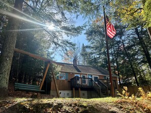 A cabin with a wooden deck, a staircase, and an American flag. - Cozy Cottage (Pickerel)