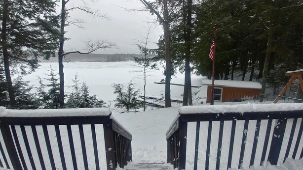 A snow-covered deck with a view of a lake and a cabin in the background. - Family friendly lakefront cottage (Pickerel)