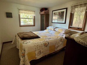 A bedroom with a bed, a dresser, two windows with curtains, and a framed picture on the wall. - Cozy Cottage (Pickerel)